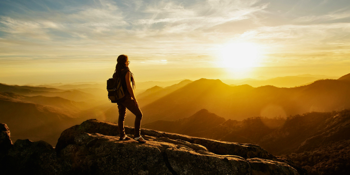 Hiker standing on a rocky overlook and watching the sun set over distant mountains.