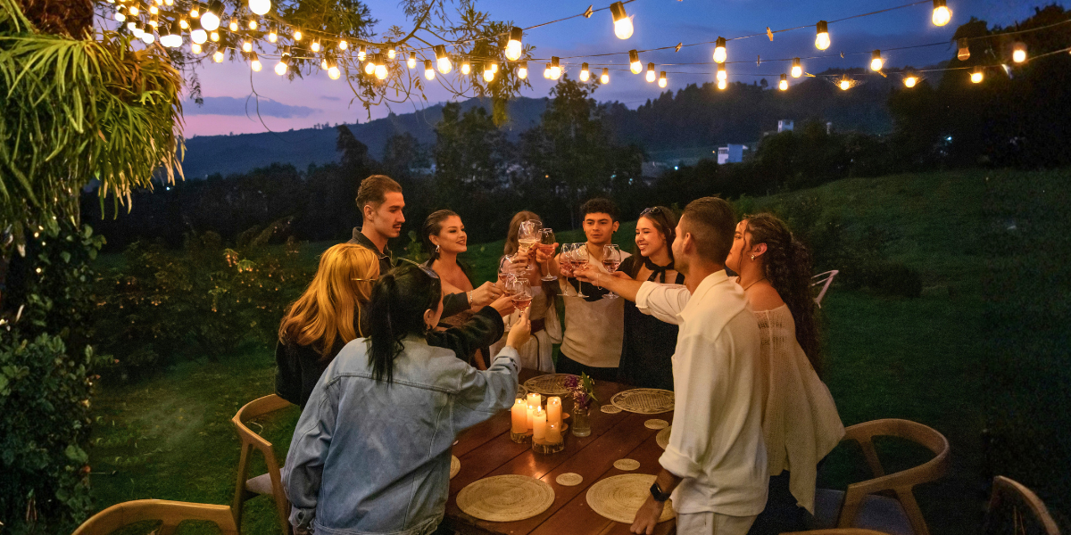 Friends raising their glasses during an outdoor dinner beneath string lights.