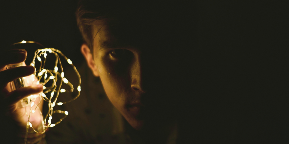 Person holding a tangled strand of glowing lights in the dark while looking toward the illuminated knots.