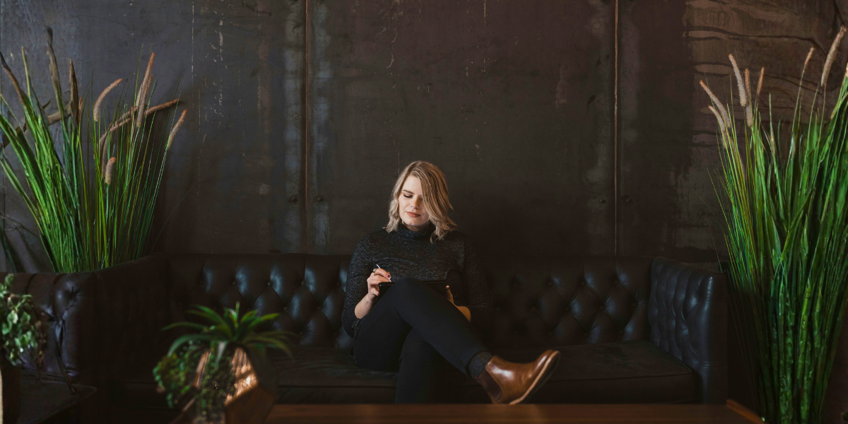 Woman sitting alone on a sofa and writing on a tablet in a quiet room.