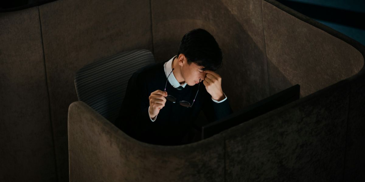 Exhausted office worker sitting alone and rubbing his eyes after removing his glasses.