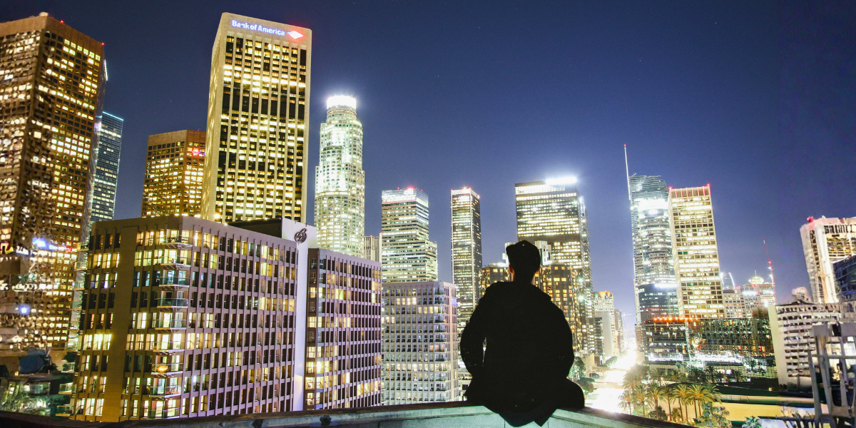 Person sitting above a brightly illuminated city skyline at night.